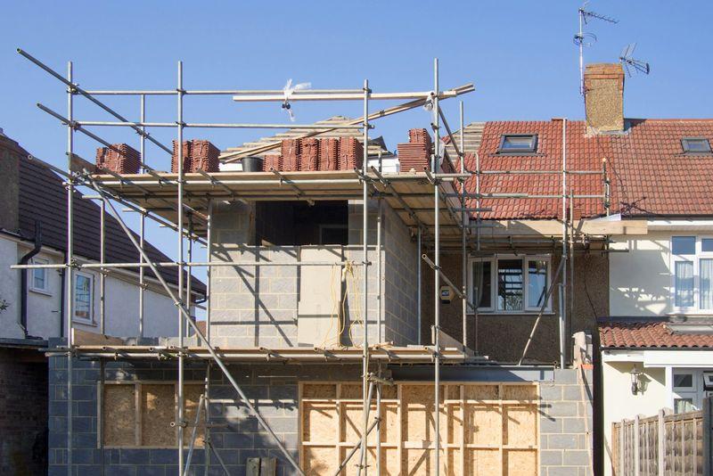 Two-story rear home extension under construction with scaffolding on a brick house