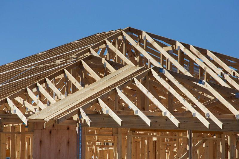 New roof truss framing of a home addition against a clear blue sky