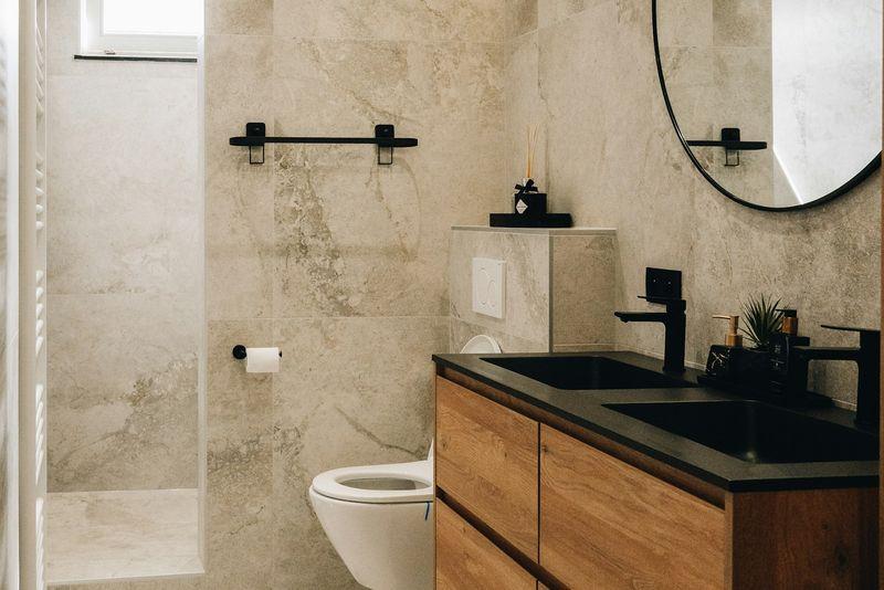 Warm travertine bathroom with wood vanity, black fixtures and round mirror