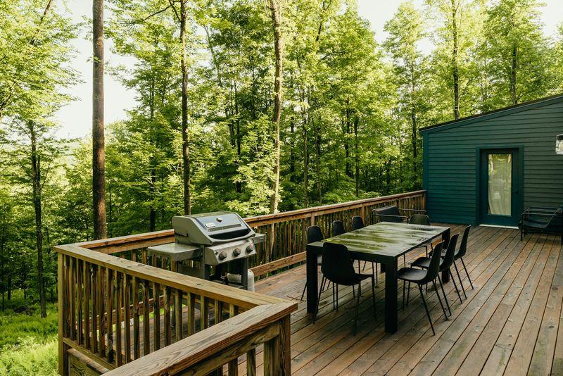 Wood deck with dining table and grill beside forest-green home