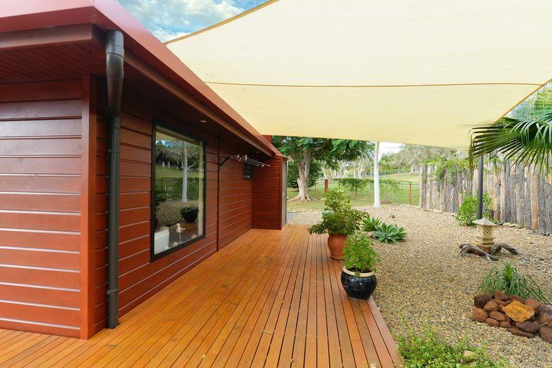 Sunlit timber deck with cream shade sail beside a home