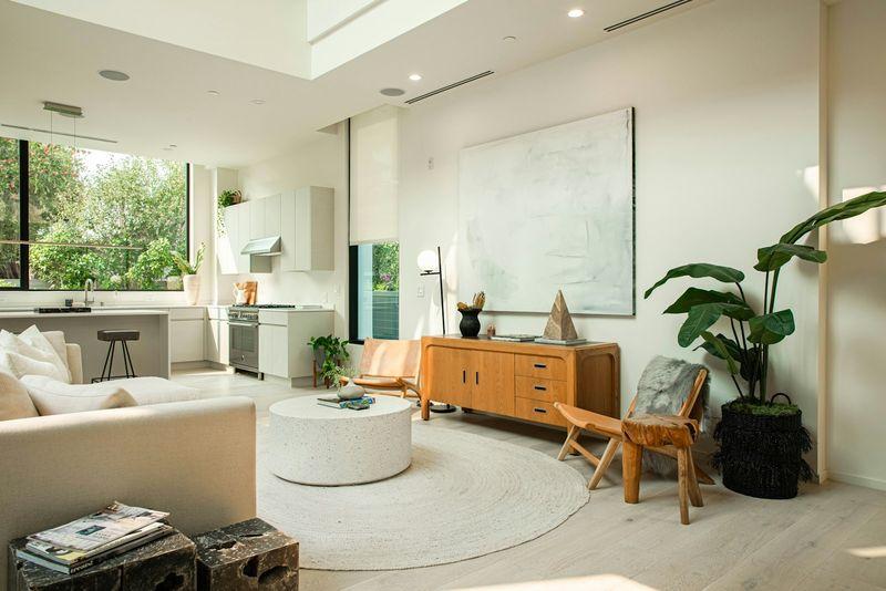 Sunlit open living room with warm wood credenza beside a renovated kitchen